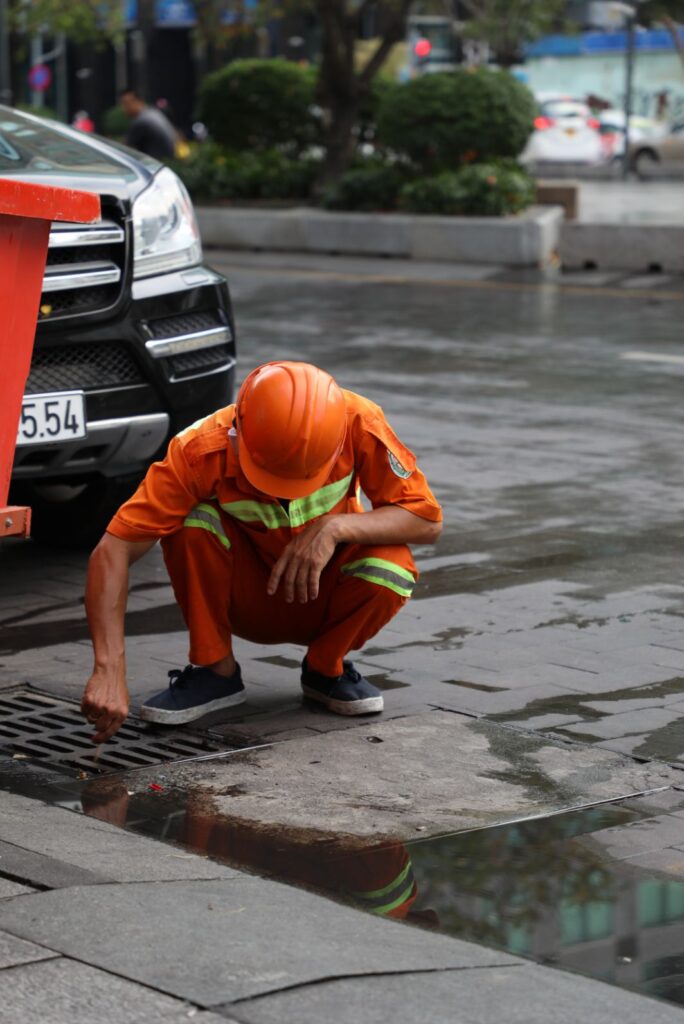 Man in Orange Jumpsuit Cleaning the Drainage